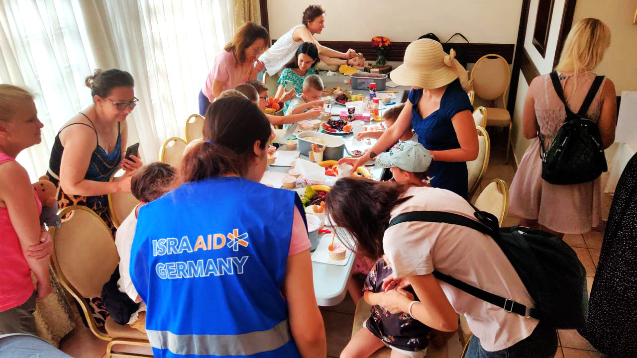 Mitarbeiterin von IsraAid an gedecktem Tisch mit ukrainischen Menschen 
