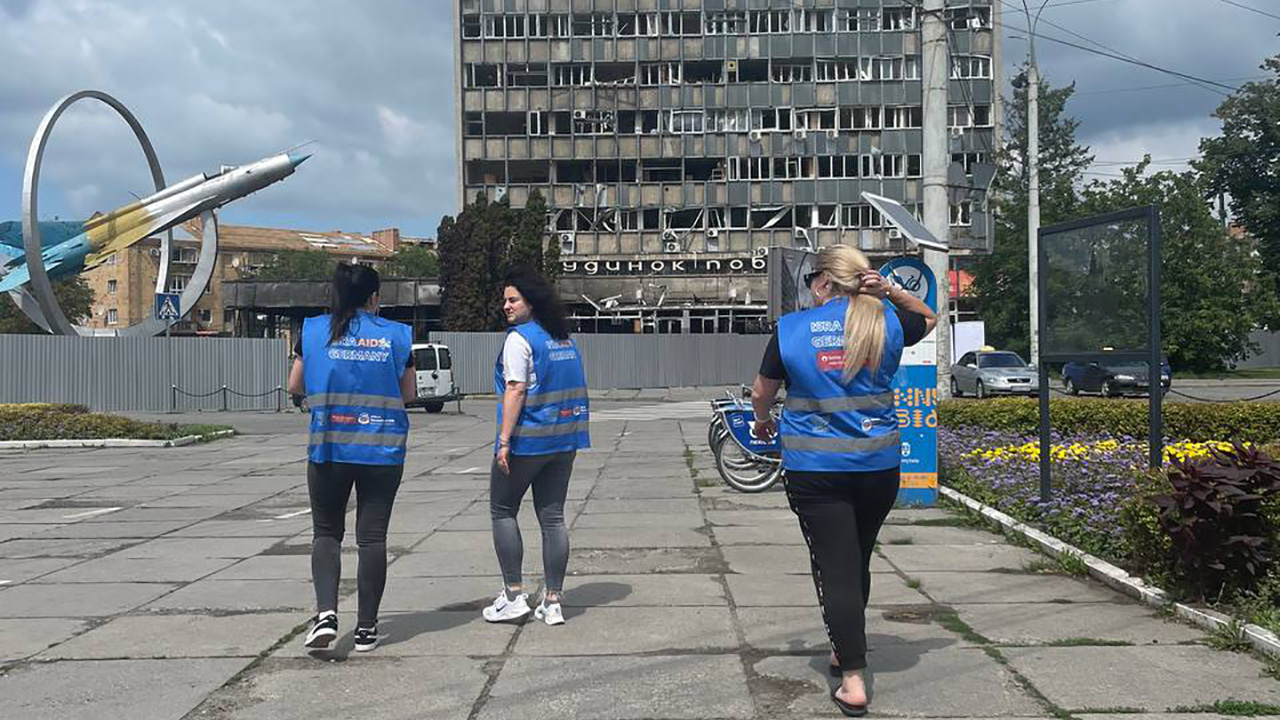 Drei Mitarbeiterinnen von IsraAid vor zerstörtem Gebäude in der Ukraine