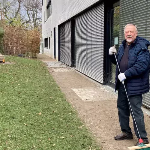 Mann mit Besen steht draußen vor einem Gebäude