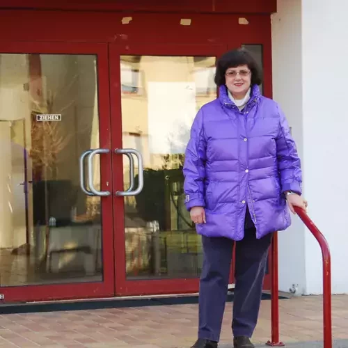 Lächelnde Frau in violettem Mantel steht vor einem gebäude