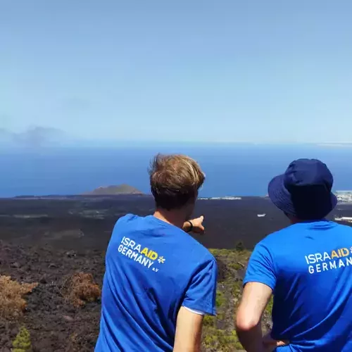 Zwei Leute stehen mit dem Rücken zum Betrachter und blicken in die Ferne auf weite Felder und Meer