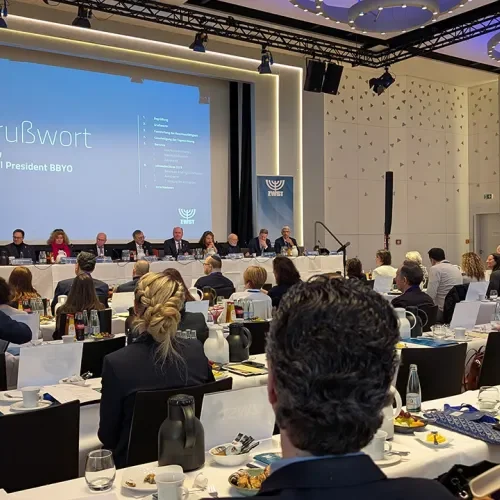 Plenum in einem Saal voller Tischreihen mit Publikum