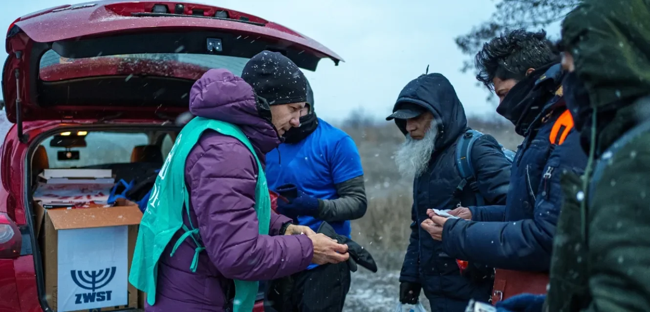 Mann übergibt drei anderen Hilfsgüter vor einem Auto