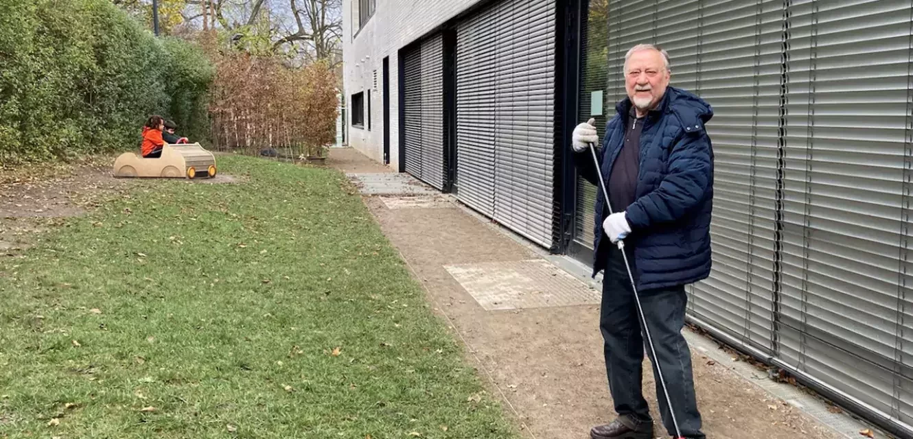 Mann mit Besen steht draußen vor einem Gebäude