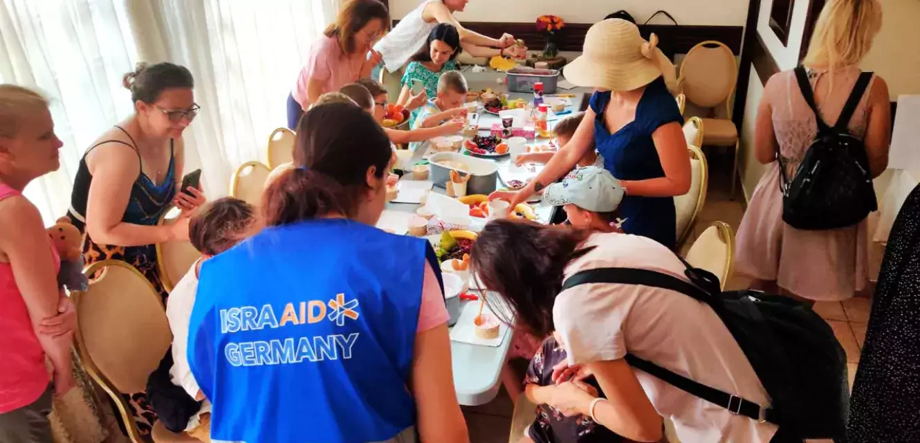 Mitarbeiterin von IsraAid an gedecktem Tisch mit ukrainischen Menschen 