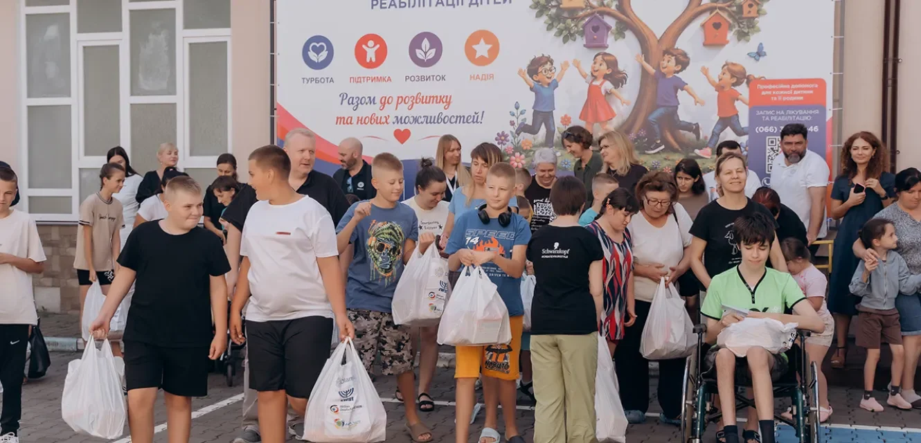 Im Vordergrund Kinder, unter anderem im Rollstuhl, mit Geschenktüten