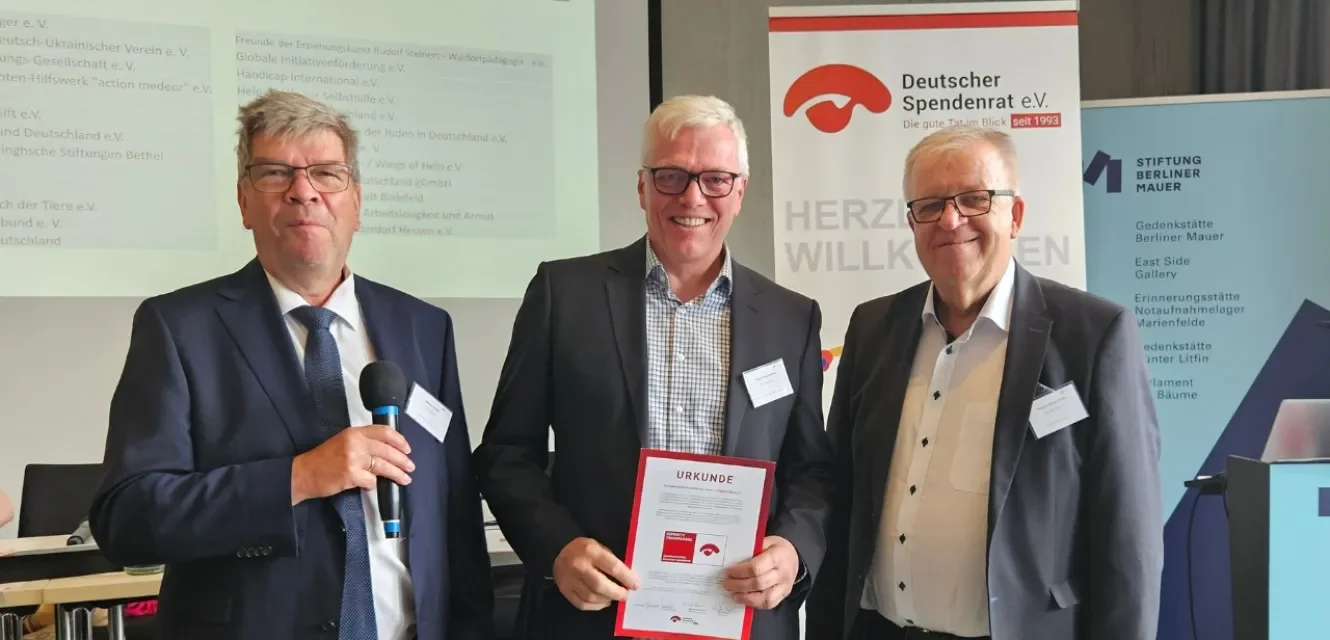 Drei Männer halten ein Spendenzertifikat