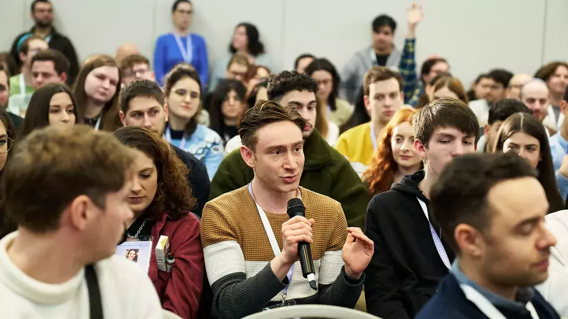 Junger Mann spricht in einem Publikum in ein Mikrophon