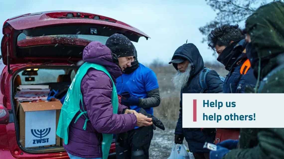 Mann übergibt drei anderen Hilfsgüter vor einem Auto