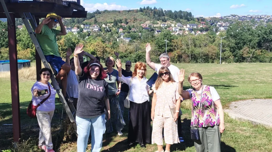 Eine Gruppe Menschen draußen in der Sonne auf einer Wiese winken